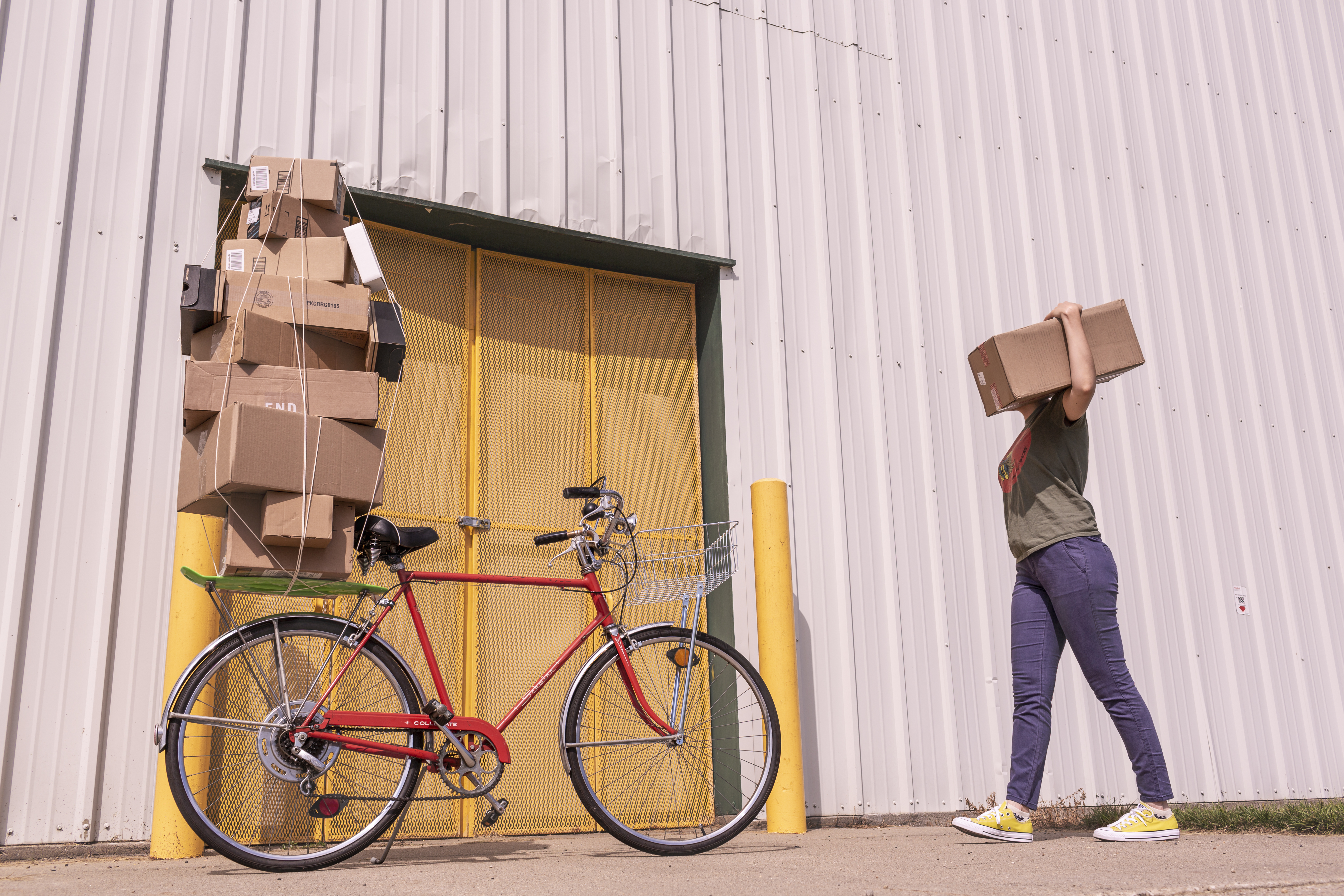 packages stacked precariously on the rack of a bike with courier carrying a package on their shoulder
